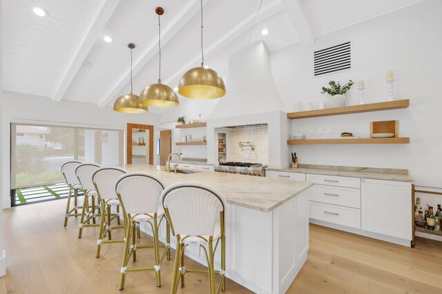 kitchen featuring a breakfast bar, sink, white cabinets, hanging light fixtures, and light stone counters