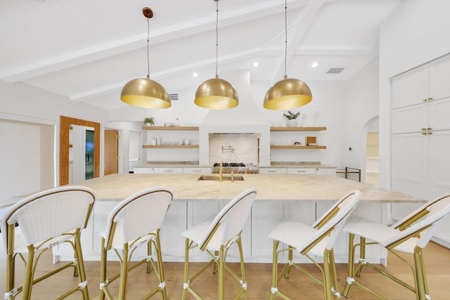 kitchen featuring pendant lighting, a breakfast bar area, white cabinetry, lofted ceiling with beams, and light hardwood / wood-style floors