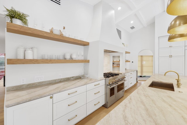 kitchen with light stone counters, sink, pendant lighting, and range with two ovens