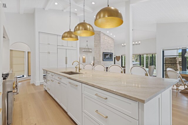 kitchen with white cabinets, a stone fireplace, sink, beamed ceiling, and a large island