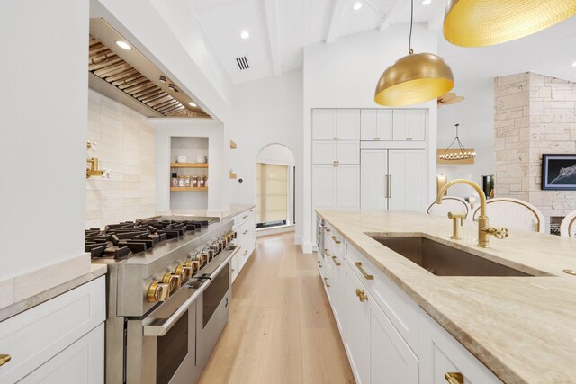 kitchen featuring sink, custom exhaust hood, decorative light fixtures, range with two ovens, and white cabinets