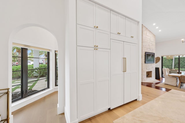 bedroom featuring light hardwood / wood-style floors, lofted ceiling, a fireplace, and multiple windows