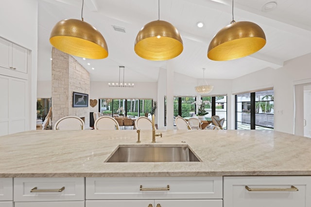 kitchen featuring white cabinetry, sink, light stone counters, and decorative light fixtures