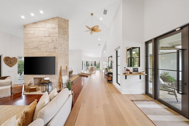 living room featuring light hardwood / wood-style floors, high vaulted ceiling, ceiling fan, and a stone fireplace