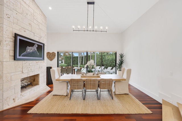 dining room featuring hardwood / wood-style flooring, a towering ceiling, a fireplace, and a chandelier