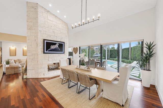 dining area featuring wood-type flooring, a fireplace, a chandelier, and high vaulted ceiling