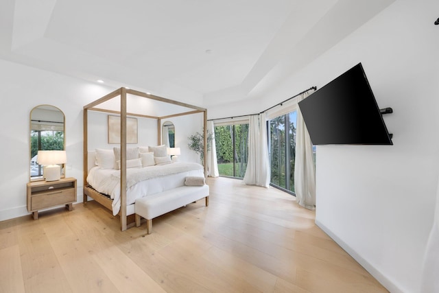 bedroom with access to exterior, a raised ceiling, and light wood-type flooring