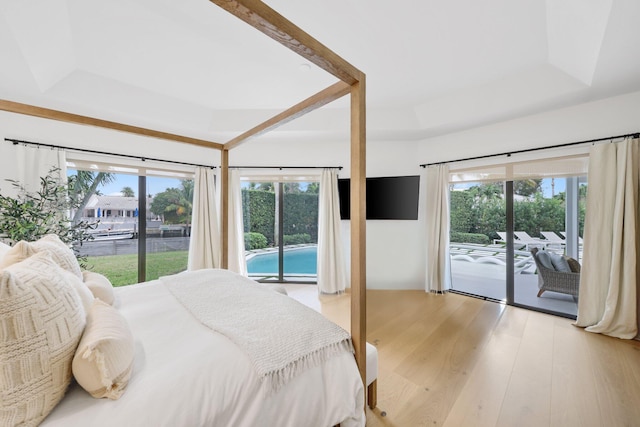 bedroom featuring access to exterior, a raised ceiling, and light wood-type flooring