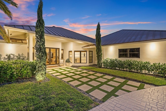 back house at dusk with a yard and french doors