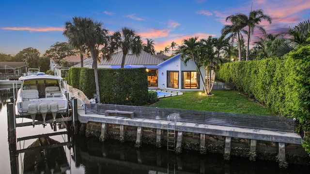 back house at dusk featuring a water view and a lawn