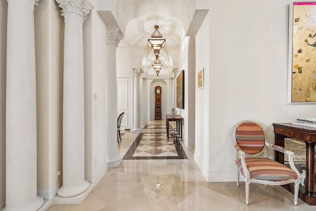 hallway featuring arched walkways, marble finish floor, decorative columns, and baseboards