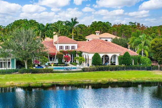 back of house with a chimney, a water view, fence, and a lawn