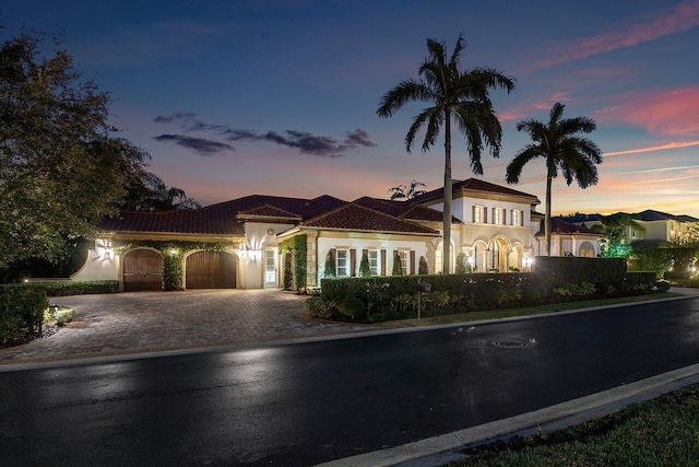 mediterranean / spanish home with decorative driveway, a tile roof, an attached garage, and stucco siding