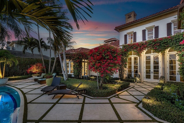 exterior space with an outdoor pool, a chimney, french doors, a patio area, and stucco siding