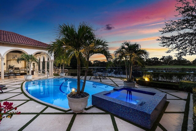 view of swimming pool featuring a water view, a pool with connected hot tub, fence, and a patio