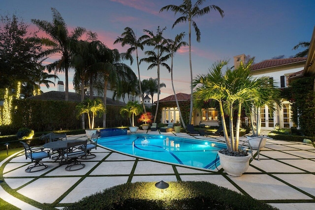 pool at dusk featuring a patio and an outdoor pool