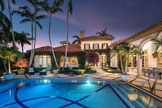 pool at dusk featuring a patio area and a hot tub