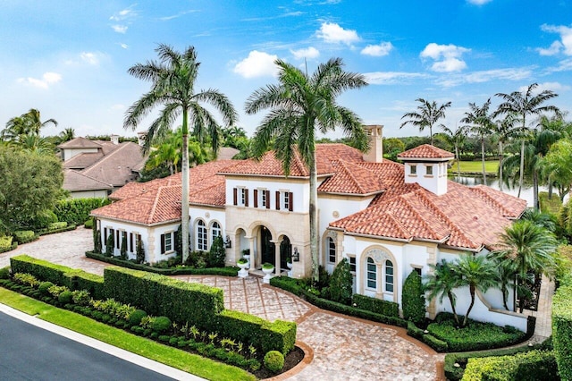 mediterranean / spanish-style house with a tile roof, a chimney, stucco siding, a water view, and driveway