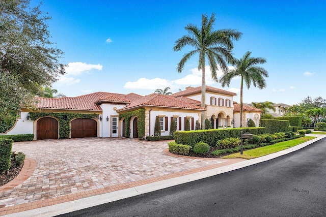 mediterranean / spanish home with a garage, a tiled roof, decorative driveway, and stucco siding