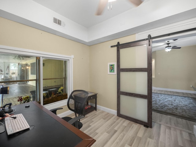 office area with a barn door, ceiling fan, and light wood-type flooring