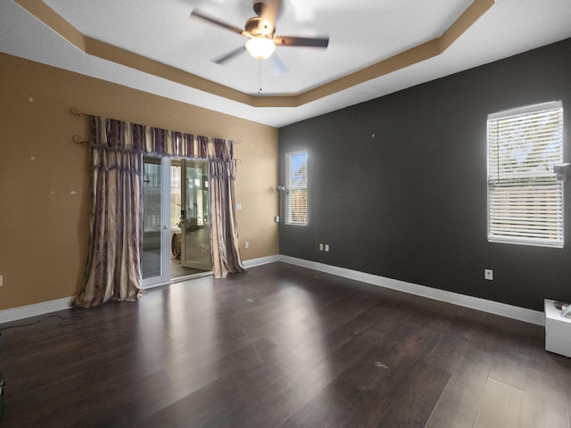 spare room with dark hardwood / wood-style flooring, a raised ceiling, plenty of natural light, and ceiling fan