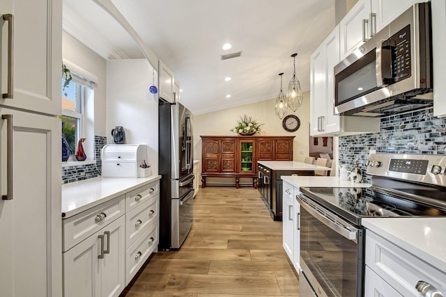 kitchen with light wood-type flooring, stainless steel appliances, white cabinetry, and ornamental molding