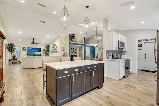 kitchen featuring white cabinets, appliances with stainless steel finishes, ceiling fan with notable chandelier, and lofted ceiling