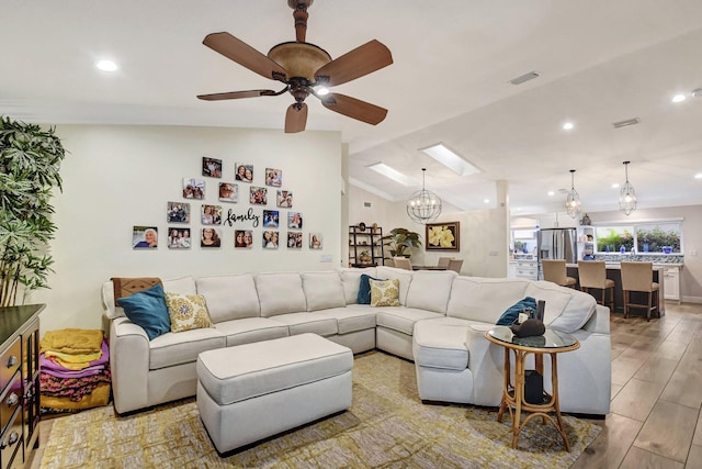 living room with ceiling fan with notable chandelier, light wood-type flooring, and lofted ceiling