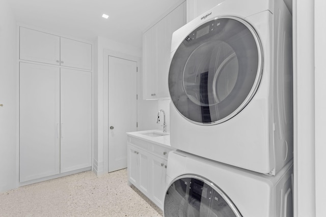 laundry room with cabinets, stacked washing maching and dryer, and sink