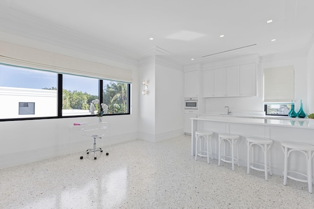 interior space with a kitchen breakfast bar, white oven, white cabinetry, and crown molding