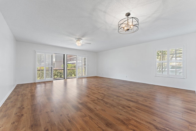 spare room with dark hardwood / wood-style flooring, ceiling fan with notable chandelier, and a textured ceiling