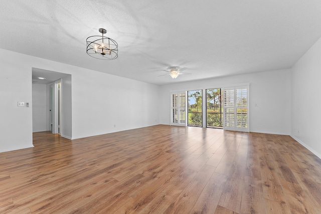 empty room with ceiling fan with notable chandelier, light hardwood / wood-style floors, and a textured ceiling