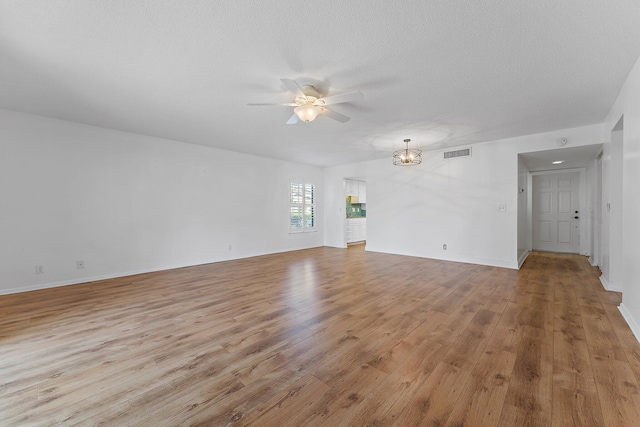 unfurnished living room featuring ceiling fan with notable chandelier, light wood-type flooring, and a textured ceiling