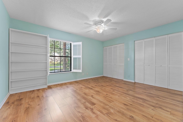 unfurnished bedroom with light wood-type flooring, a textured ceiling, ceiling fan, and multiple closets