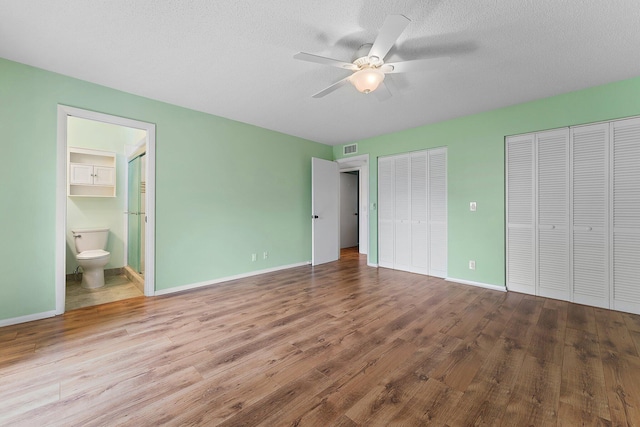 unfurnished bedroom featuring connected bathroom, ceiling fan, multiple closets, light hardwood / wood-style flooring, and a textured ceiling