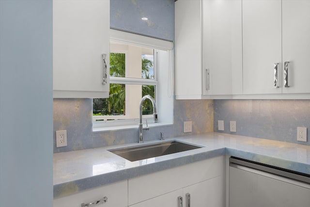 kitchen with backsplash, dishwashing machine, white cabinetry, and sink