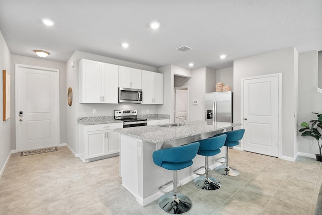 kitchen featuring appliances with stainless steel finishes, a breakfast bar, sink, a center island with sink, and white cabinetry