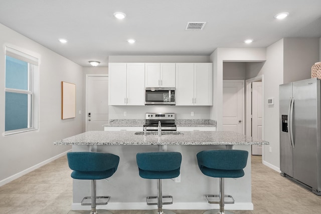 kitchen with light stone countertops, a kitchen breakfast bar, stainless steel appliances, a kitchen island with sink, and white cabinetry