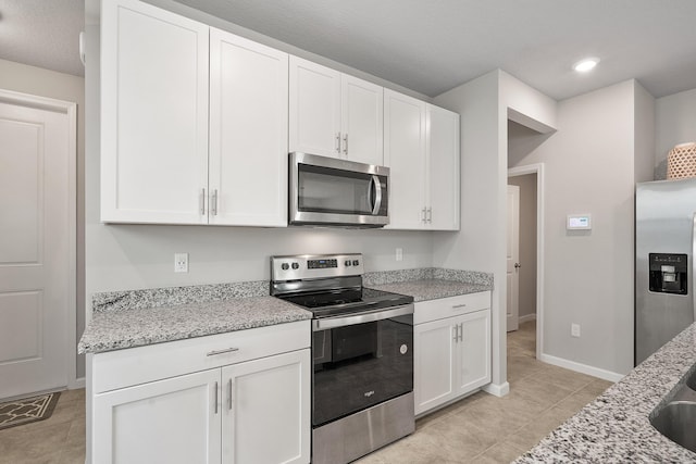 kitchen with light stone countertops, white cabinetry, light tile patterned floors, and stainless steel appliances