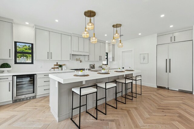 kitchen with light parquet flooring, a center island, wine cooler, and hanging light fixtures