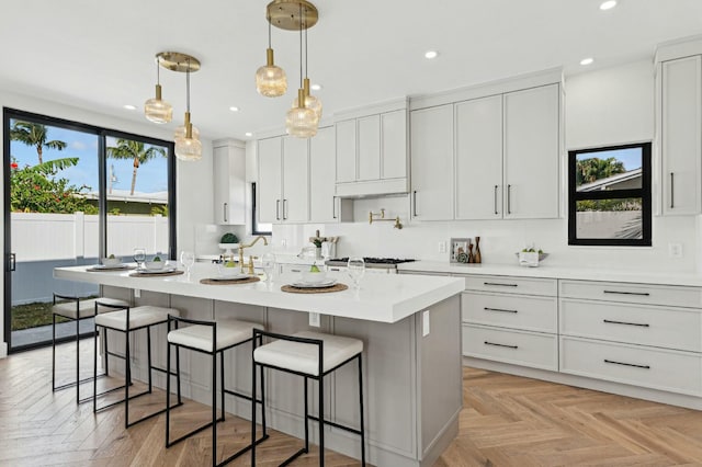 kitchen with a center island, hanging light fixtures, white cabinets, a breakfast bar area, and light parquet flooring