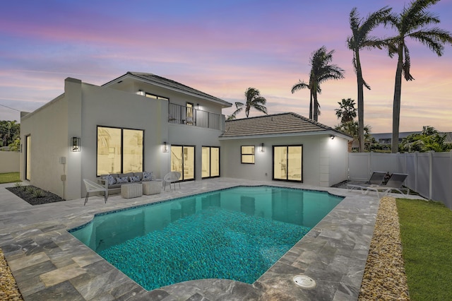 back house at dusk featuring a fenced in pool, a patio area, outdoor lounge area, and a balcony