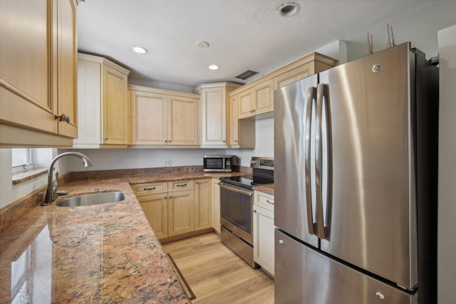 kitchen with light brown cabinets, sink, light wood-type flooring, light stone counters, and stainless steel appliances