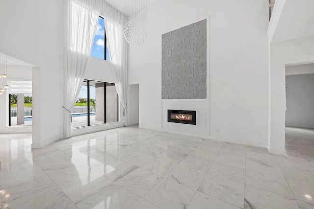 unfurnished living room featuring a large fireplace, a towering ceiling, and a chandelier