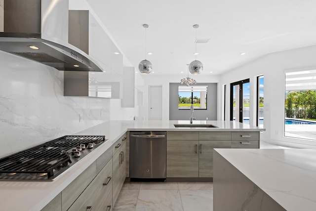 kitchen with sink, wall chimney range hood, backsplash, pendant lighting, and appliances with stainless steel finishes