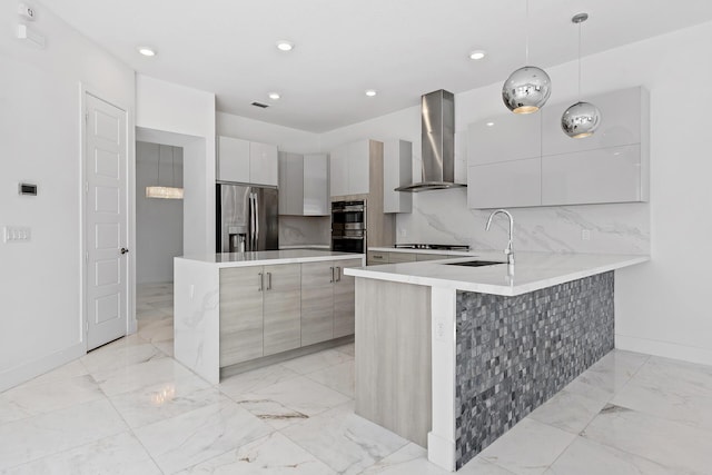 kitchen with sink, wall chimney range hood, kitchen peninsula, decorative light fixtures, and appliances with stainless steel finishes