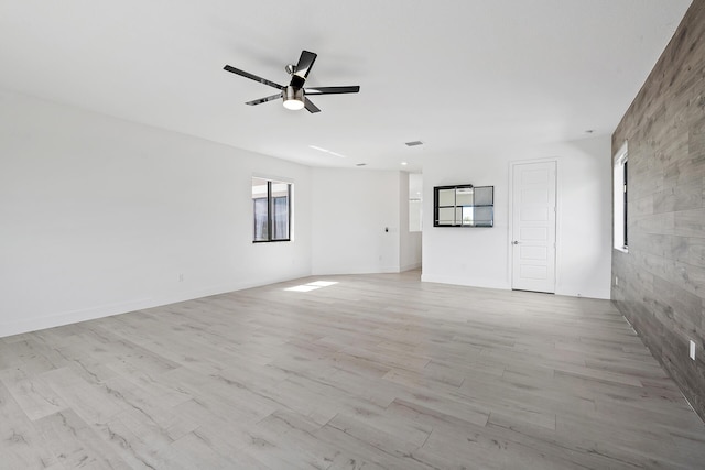 unfurnished living room featuring light hardwood / wood-style flooring, tile walls, and ceiling fan