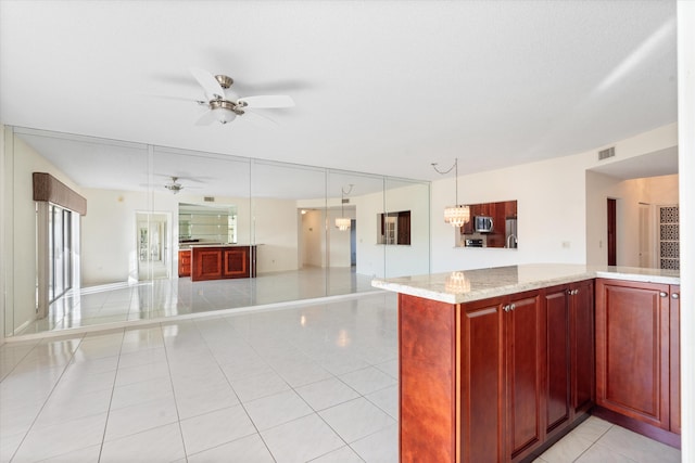 kitchen featuring light stone counters, light tile patterned floors, hanging light fixtures, and ceiling fan with notable chandelier