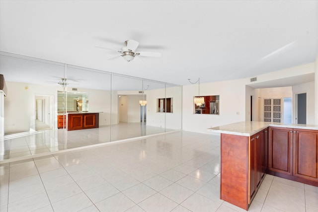 kitchen with light stone countertops, stainless steel refrigerator with ice dispenser, pendant lighting, light tile patterned floors, and ceiling fan with notable chandelier