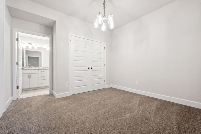 unfurnished bedroom with ensuite bath, sink, an inviting chandelier, light colored carpet, and a closet